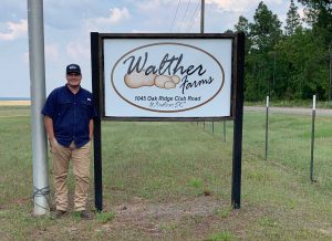 Photo of Paul Hawkins next to sign reading "Walther Farms 1045 Oak Ridge Club Road Windsor South Carolina"