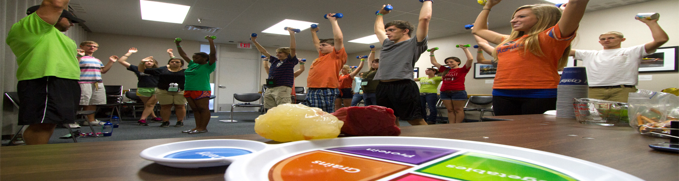 Young people lifting weights for physical activity with USDA MyPlate, pound of fat model, and pound of muscle model in foreground