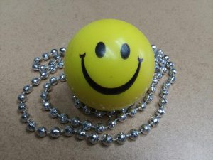 Yellow squishy ball with smiley face surrounded by silver bead necklace