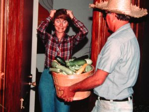 A woman looks overwhelmed as a man brings her a bushel of squash.