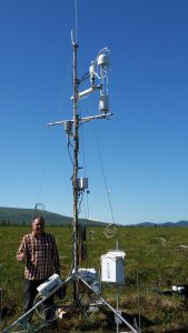 researcher standing with data collection tower in the arctic in the summer