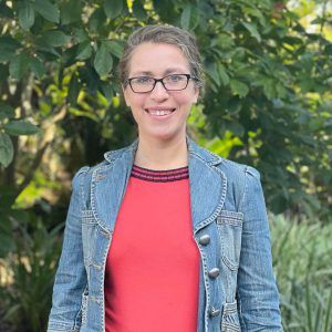 Rachel Mallinger looks into the camera and smiles, behind her is green foliage/