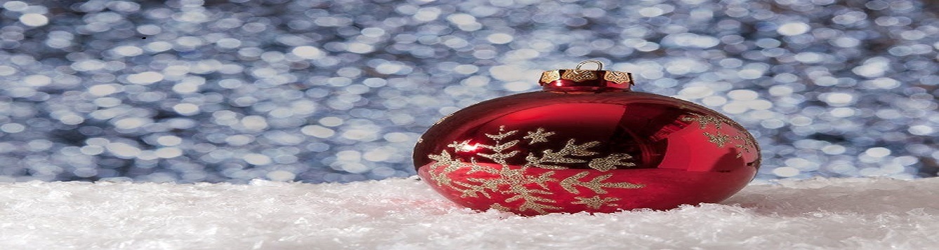 A red Christmas ornament laying in the snow while snow is falling