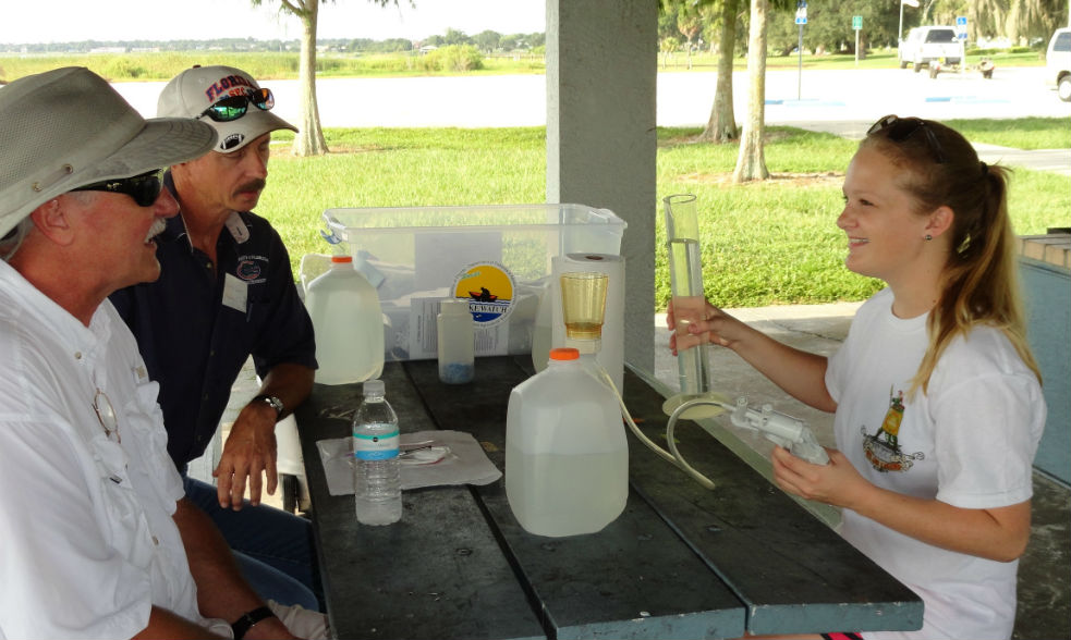 A women demonstrates to two men how to process an algae sample in the field as a part of Lakewatch training.