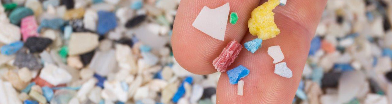 Close-up photo of microplastic pieces with two fingers for scale.