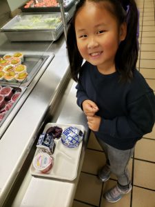 an elementary age girl standing with her lunch tray with purple sweet potatoes on plate