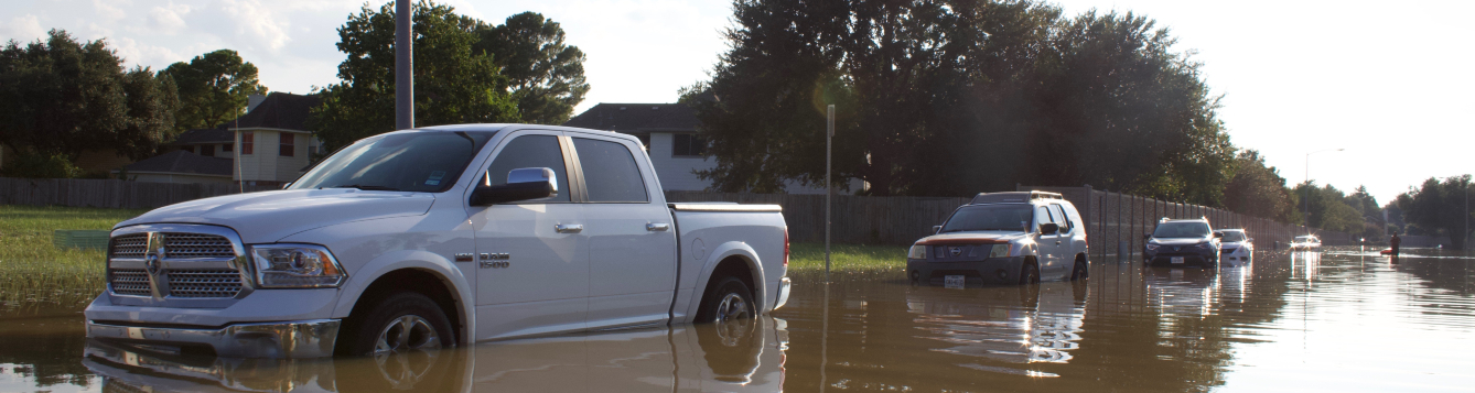 a row of vehicles sit in standing water on a flooded neighborhood road