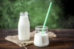 A glass of milk with a green straw sits in front of a small jug of milk, in an outdoor setting.. [CREDIT: pixabay.com, Imo Flow]