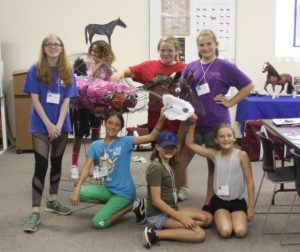 Seven girls standing next to model wire horse that they have created a disgestive track for