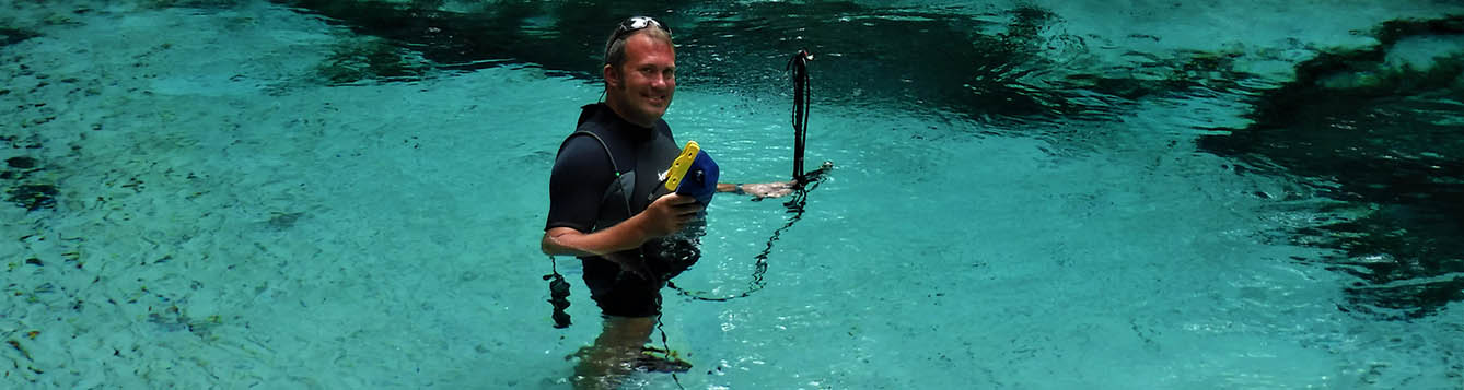 Man in wetsuit standing in Florida spring pool with measurement equipment