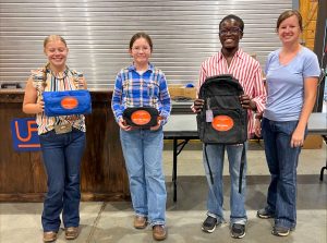 3 youth holding up prizes they won for livestock judging next to coach Allyson Trimble