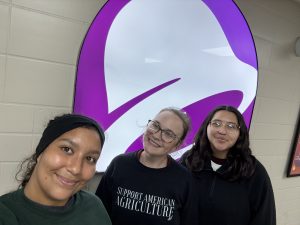 Three girls posing for a group picture in front of the Taco Bell logo