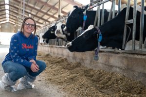 Girl posed next to dairy cows eating inside barn