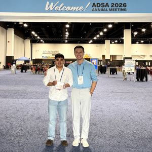 Angelo Castro holds an award and stands next to Dr. Haipeng Yu in front of a blue welcome banner for the ADSA 2026 annual meeting. 
