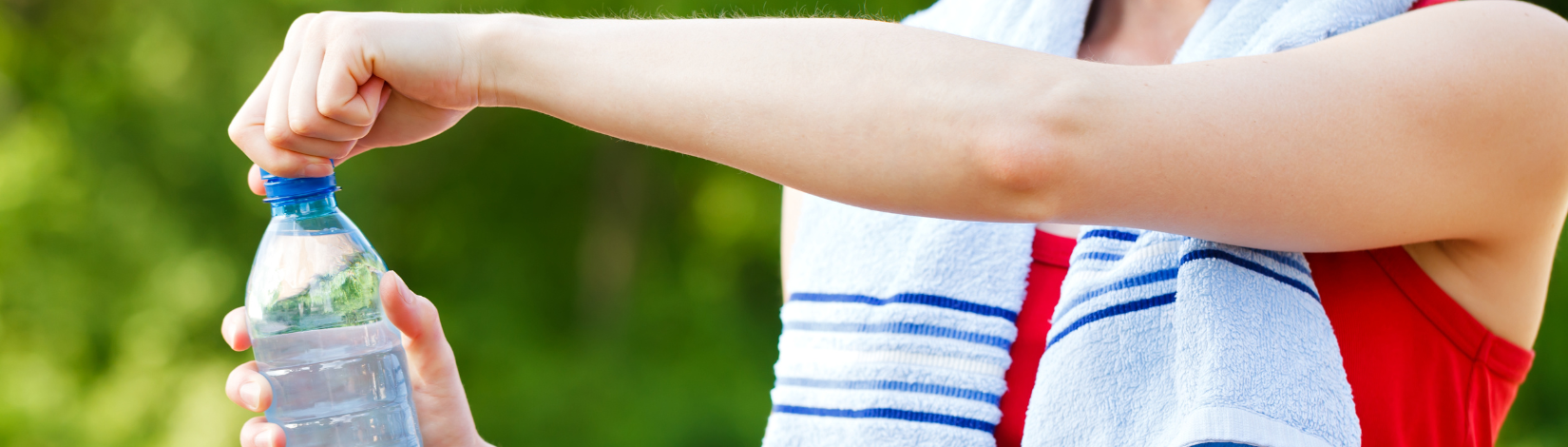 Image of person wearing a tank top with a towel around the shoulders. This person is opening a water bottle.