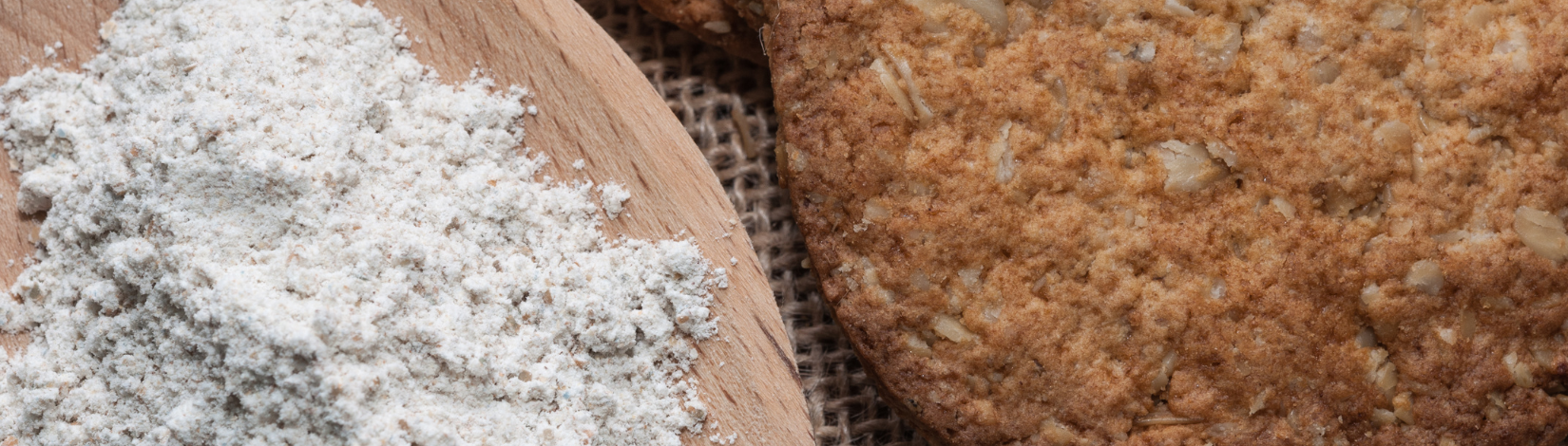 A wooden spoon with baking flour on it. next to a cookie