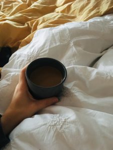 hand holding a cup of coffee over blankets