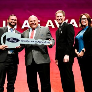 Four people standing in a line. Holding a large key that reads "Ford. Excellence in Agriculture."