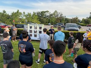A man in a blue shirt and khakis in front of a group of volunteers discussing tree planting