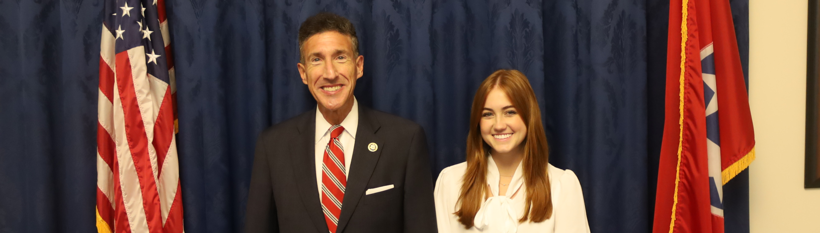 Student with legislator in front of flags.
