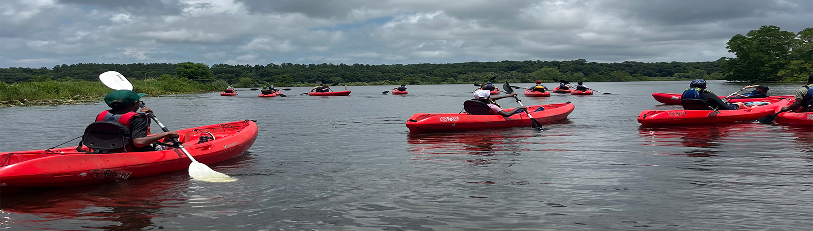 4-H campers kayaking in red kayaks on a lake.
