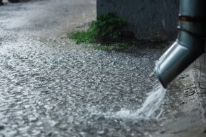 downspout pouring rainwater onto paved surface