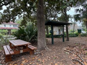 A picnic table, kiosk and free library stand in a park