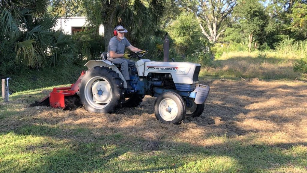 man on tractor tilling a garden plot whose cover crop has already been mowed down
