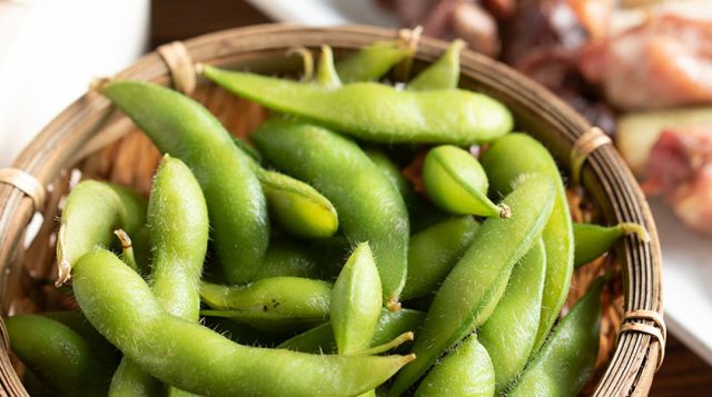 Bowl of boiled edamame pods served with two other dishes.