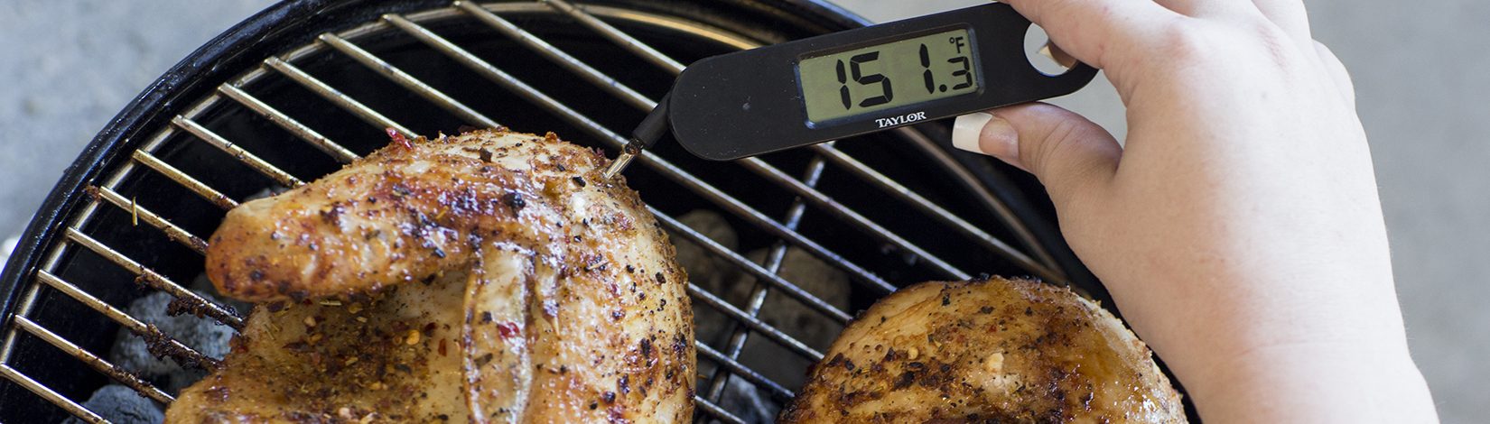 Person uses meat thermometer to check doneness of chicken while grilling.