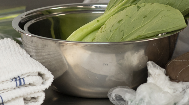 Metal bowl of mixing greens on a kitchen preparation table among other kitchen necessities.