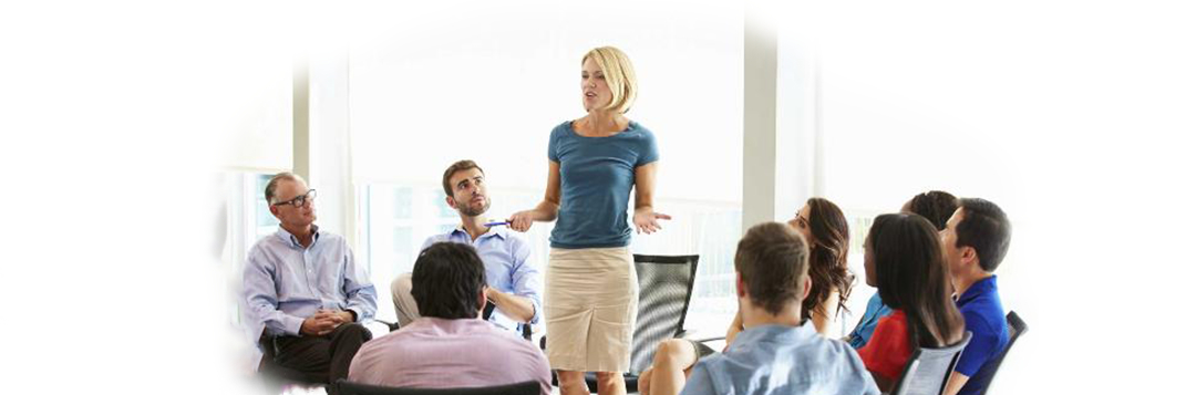 woman stands on chair to share story with circle of listeners in office setting