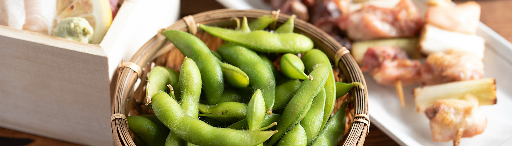 Bowl of boiled edamame pods served with two other dishes.