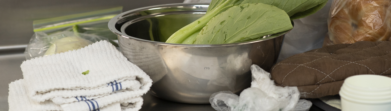 Metal bowl of mixing greens on a kitchen preparation table among other kitchen necessities.