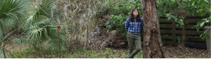 Woman stands near a dead tree in a yard.