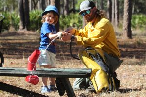 A man shows a child how to use a fire hose.