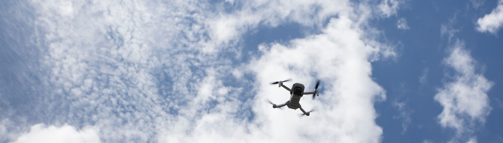 An unmanned aerial vehicle, or drone, flies overhead in the sky.