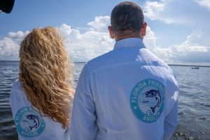 A woman, left, and a man, right, stand in a boat looking out over the water while wearing Florida Friendly Angler program longsleeve button-down shirts.