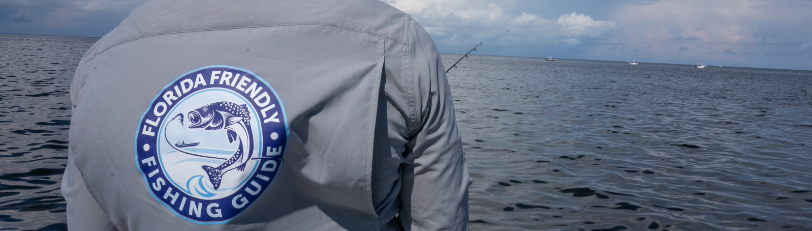 An angler wearing a Florida Friendly Fishing Guide longsleeve button-down shirt fishes while standing in a boat.