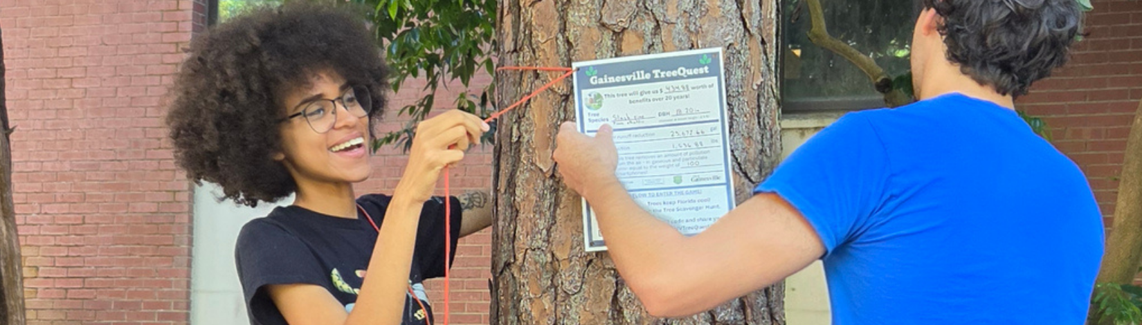 Young woman ties a sign to a tree.