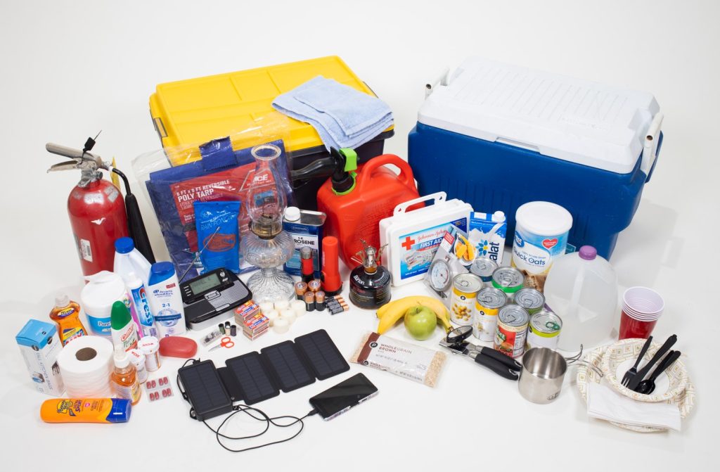 Supplies for a hurricane preparation kit, including a cooler, canned food, and a solar powered battery backup. 