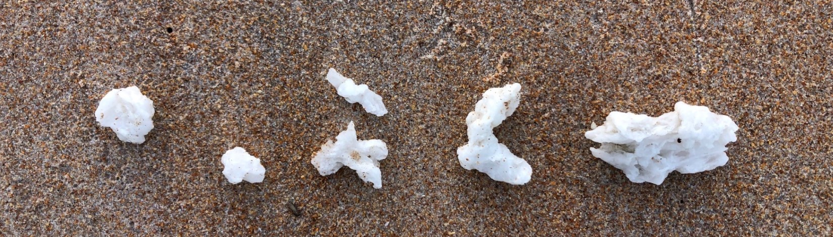 White irregular shaped balls of wax set on the sand of the beach