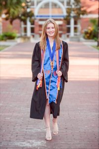 FRE graduate Emerson Searl poses in front of stadium in commencement regalia.