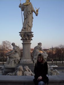 Gozde wearing a black coat and sitting on the edge of a fountain in Vienna, Austria.