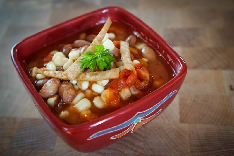 Bean and veggie chili served in a small, square red bowl.