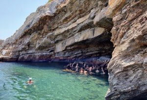 A group of people swim in green-blue waters next to a large cliff.