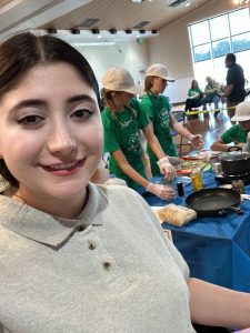 Razieh wearing a white sweater in front of a room full of people.