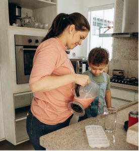 Child and adult preparing and serving a smoothie in the kitchen.