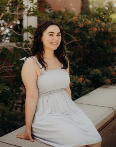 Courtney sits outside and wears a white dress.