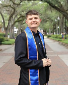 Eleazar Torres UF standing outside in his graduation robes.